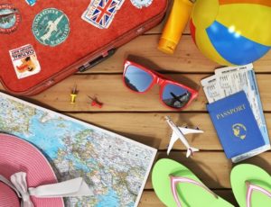 sunglasses, world map, beach shoes, sunscreen, passport, planeickets, beach ball, hat and old red suitcase for travel on the wood background.